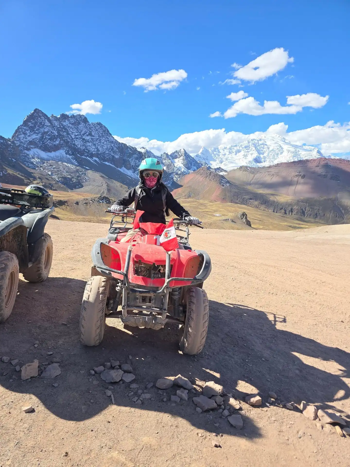 Travelers riding ATVs along a dirt track with the striped slopes of Rainbow Mountain behind them