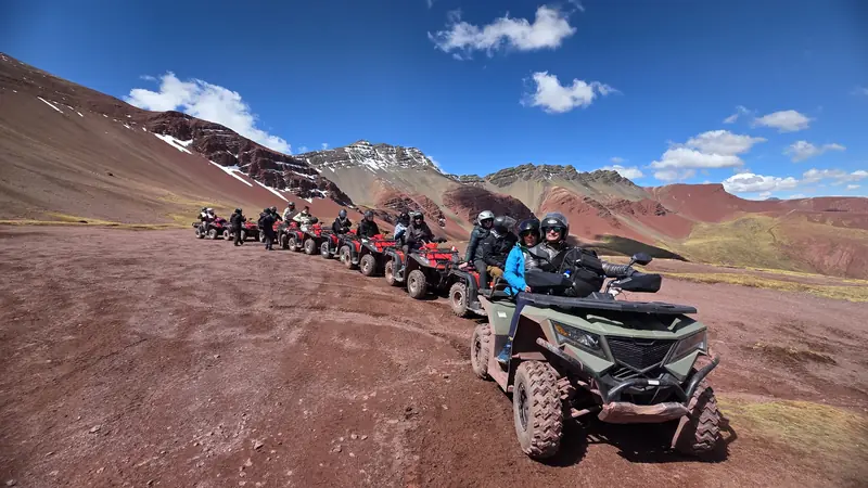 A column of quad bikes climbing the track towards Vinicunca with the striped ridge behind