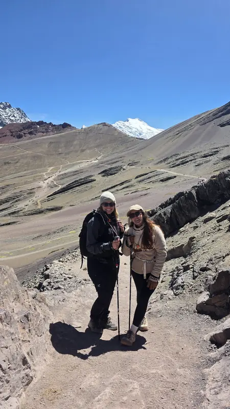 Two travelers on the path with the coloured mountain behind them